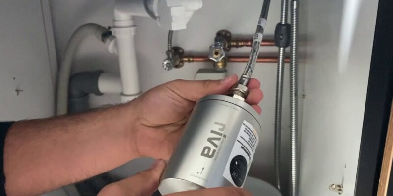 Das Bild zeigt eine Person, die einen Wasserfilter unter einem Waschbecken in der Küche installiert. Der riva Wasserfilter wird an die Wasserleitung angeschlossen.